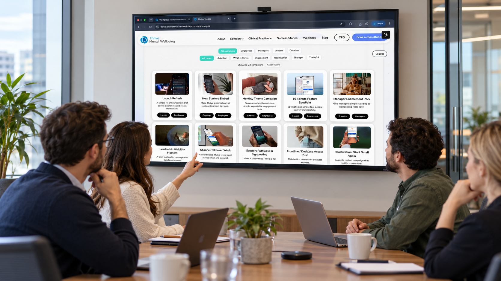 A small workplace team reviewing the Thrive campaign library on a conference-room display